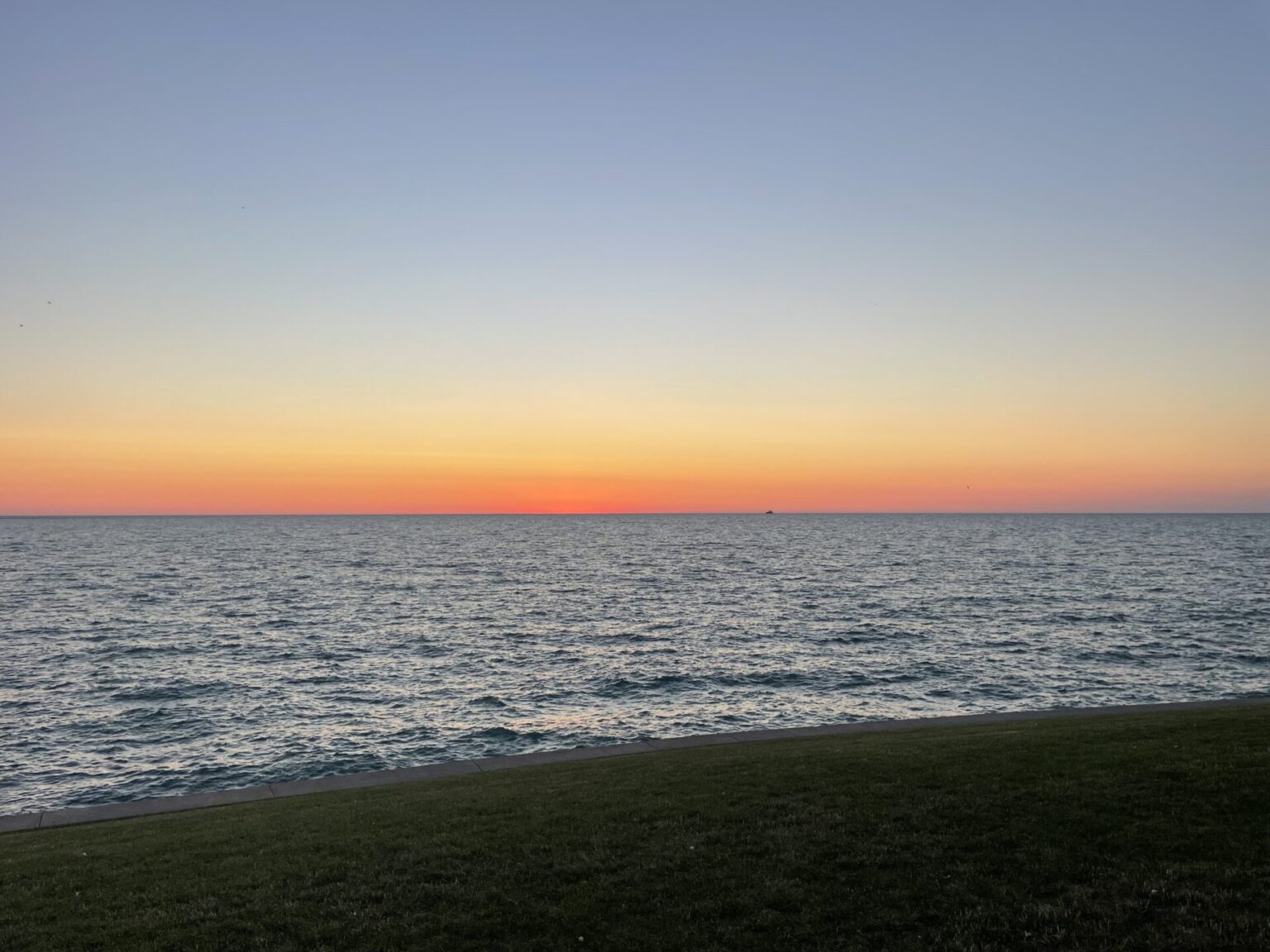 Orange and pink predawn sky over Lake Michigan, viewed from the grassy shoreline at Northerly Island.