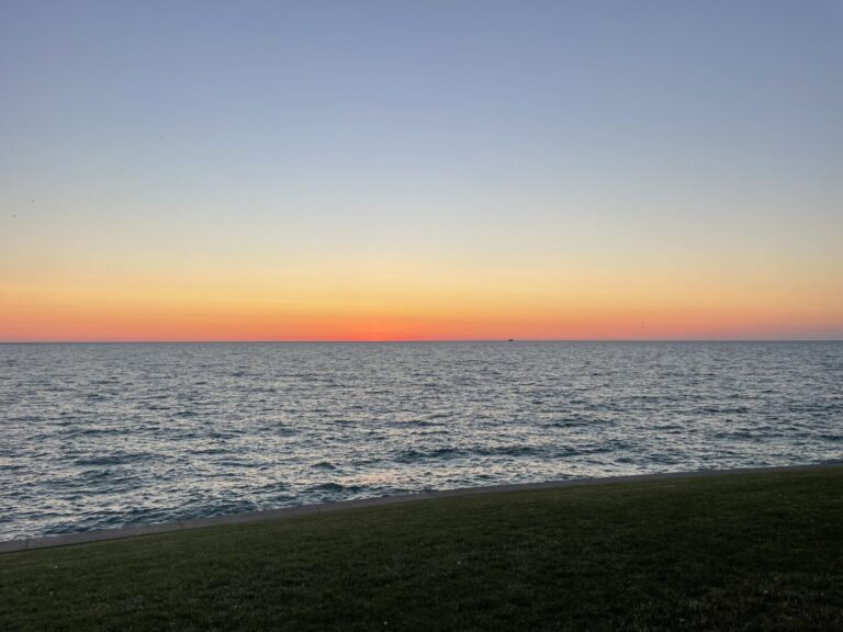 Orange and pink predawn sky over Lake Michigan, viewed from the grassy shoreline at Northerly Island.