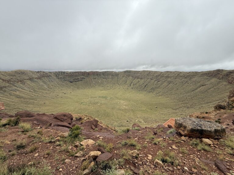 Wide view across Meteor Crater in Arizona, showing its enormous bowl-shaped floor and steep rocky walls.