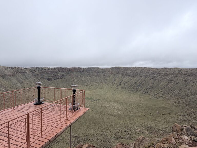 Viewing platform overlooking Meteor Crater in Arizona, with the crater floor and rocky walls beneath a cloudy sky.