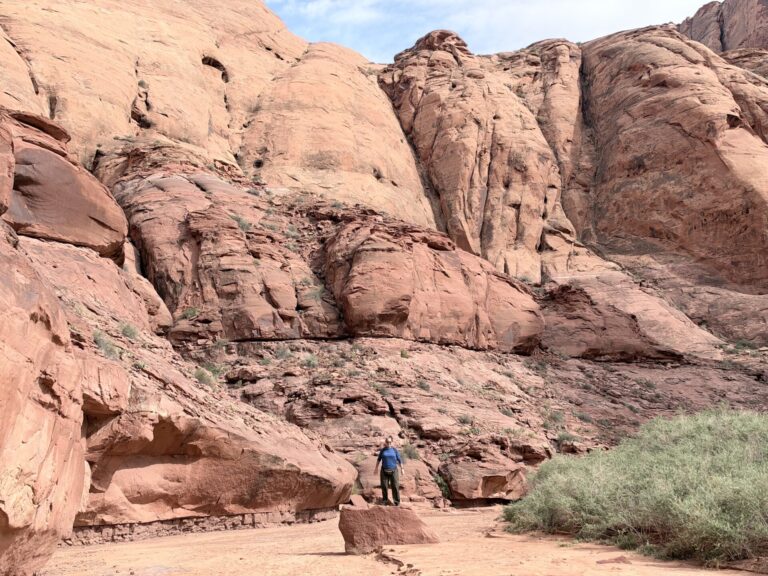Stephanie standing below towering red sandstone cliffs in Glen Canyon near the Colorado River in Arizona